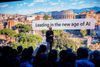 microsoft ceo satya nadella speaks to a crowd in front of a slide that says "leading in the new age of ai"