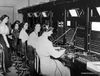 operators from the early days of telephones sit in front of a bank of connections, helping place calls