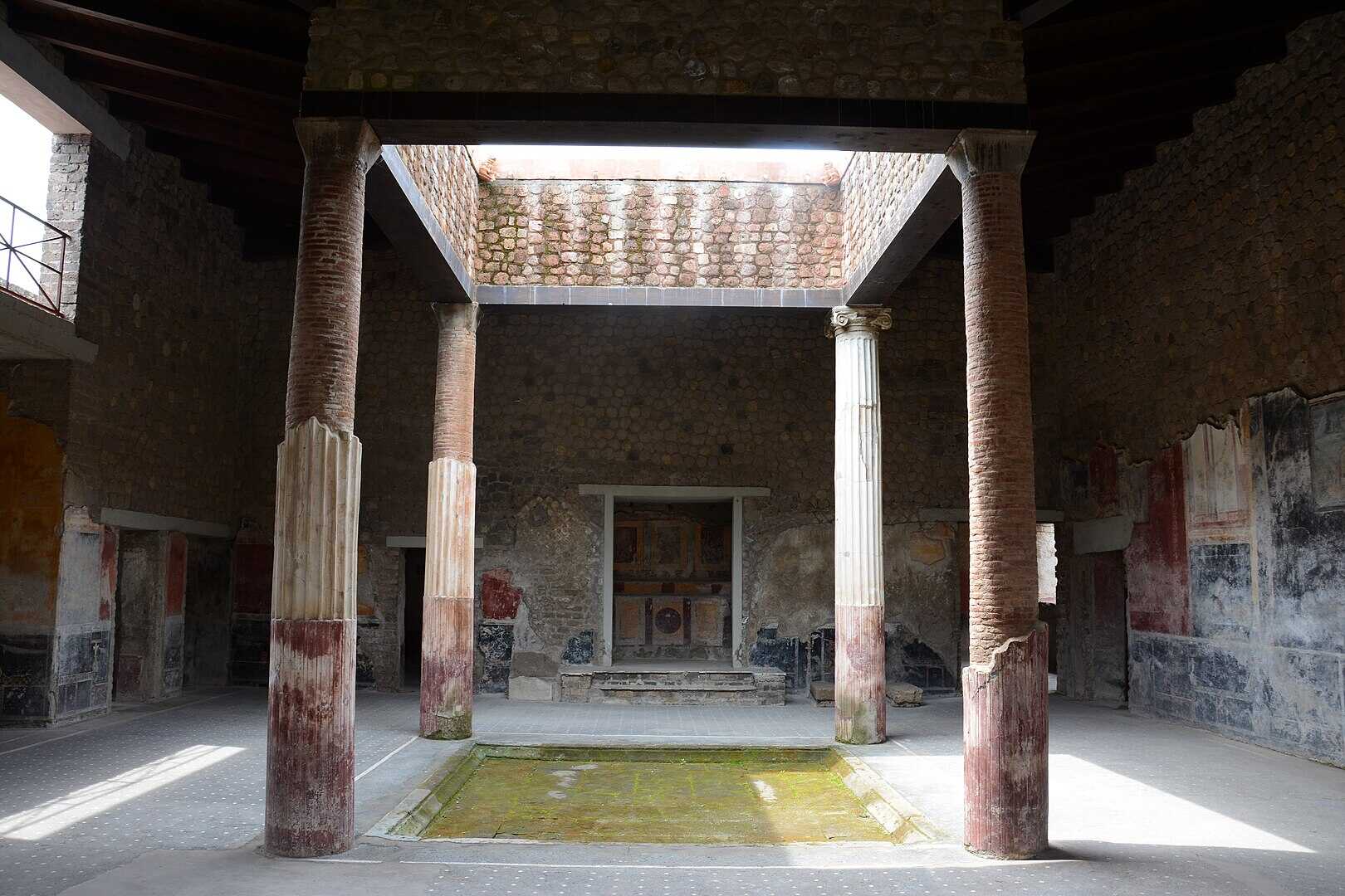 The larger tetrastyle atrium of the Villa San Marco, Stabiae; four pillars support the roof. The central niche is the lararium; the two blocks of limestone (behind the pillar with the near-intact stucco) supported the arca, a strongbox or safe
