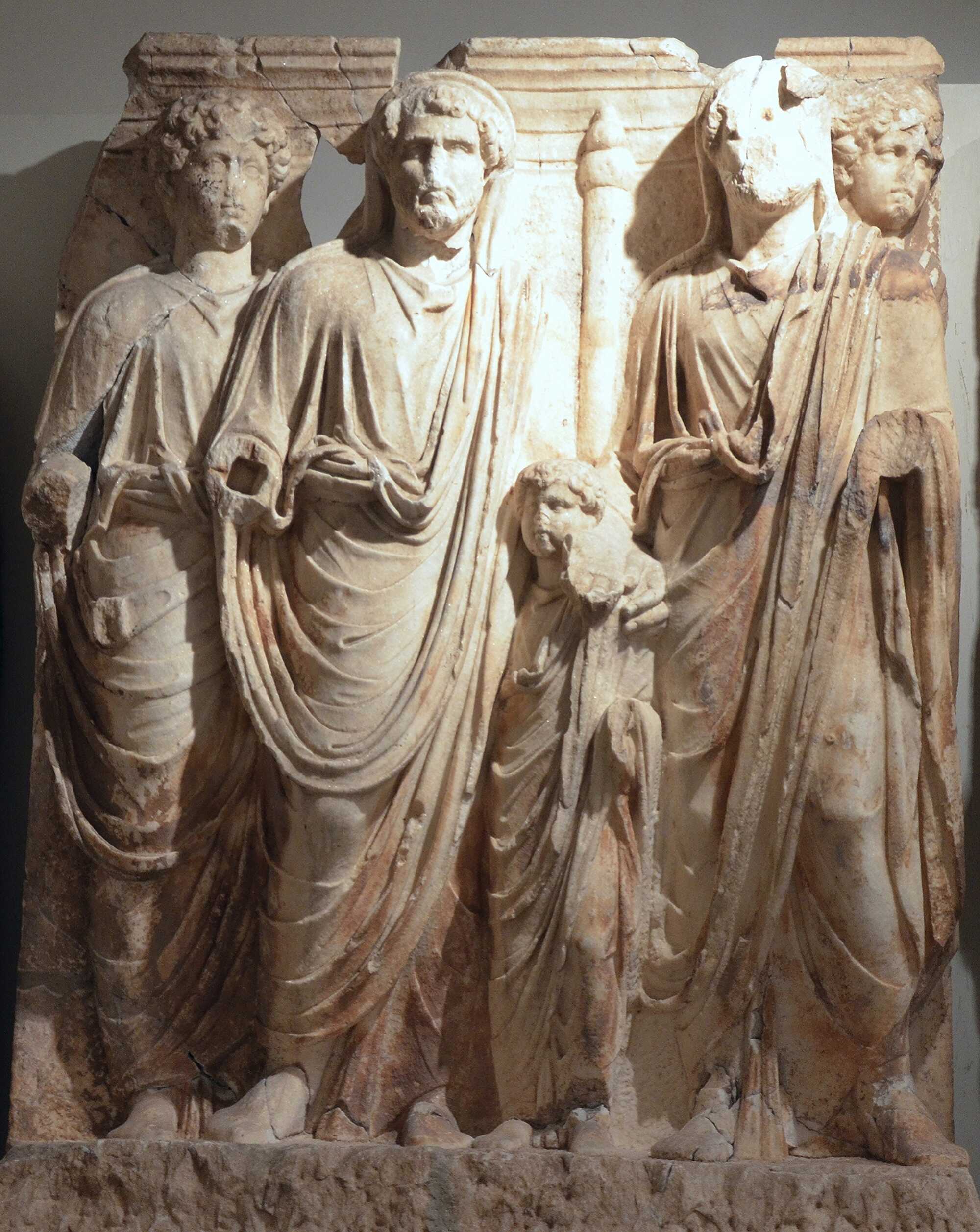 During his reign the Emperor Hadrian (figure right) adopted Antoninus Pius (centre left) and he in turn adopted the 17 year old Marcus Aurelius (left) and the 8 year-old Lucius Verus. A head stares from behind Hadrian’s left shoulder, presumably representing the guardian spirit of Aelius Verus, the late father of Lucius. The sacrifice of a bull is being offered to the gods.