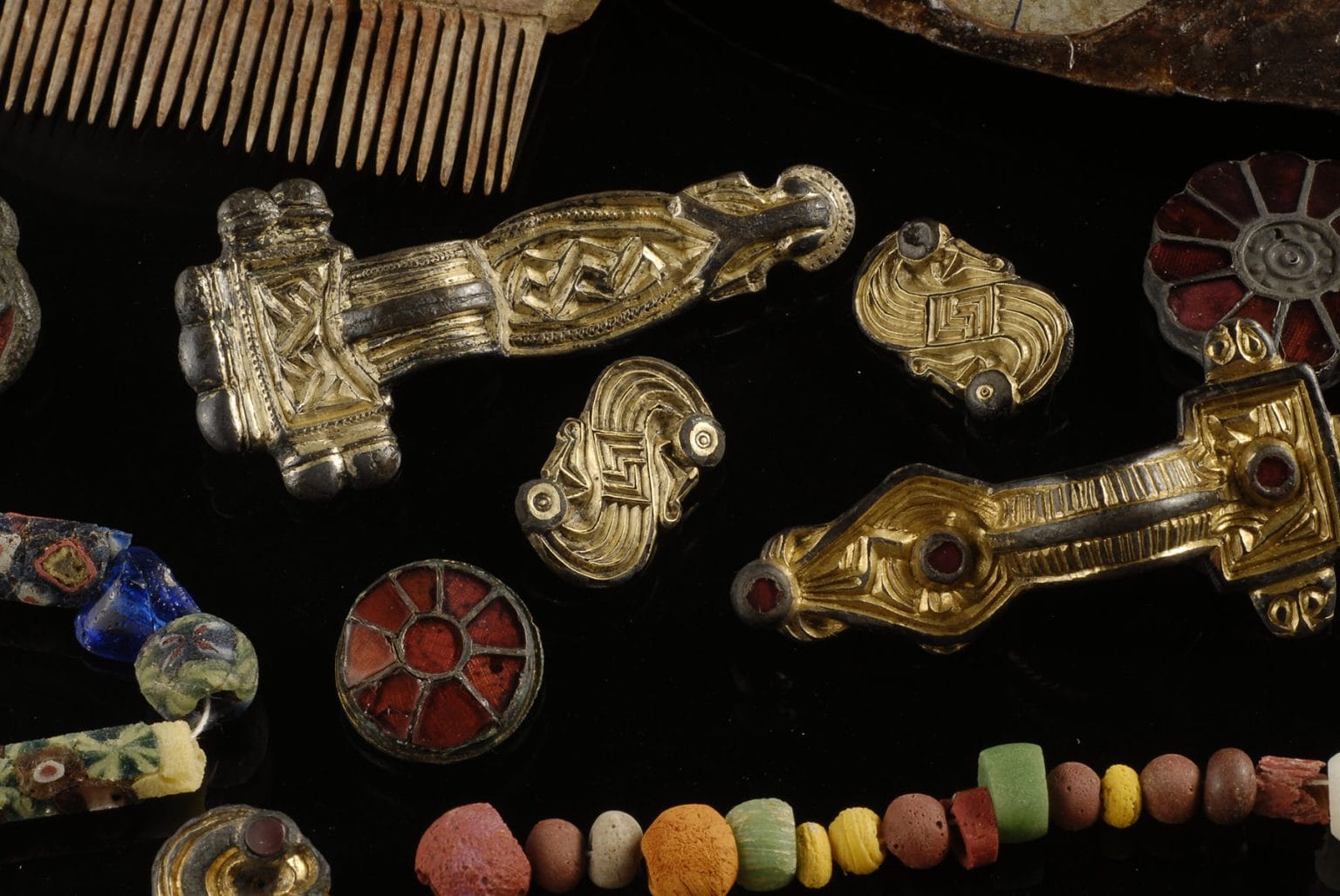 This collection of grave items from Szeleste features the center of a shield, or umbo (upper right), various brooches (center), mosaic beads, and an antler comb (top left)