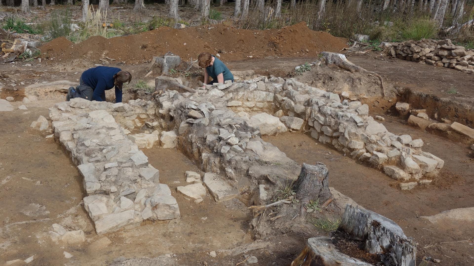 Two archaeologists working beside exposed stone foundations at the Roman temple excavation near Kapersburg.