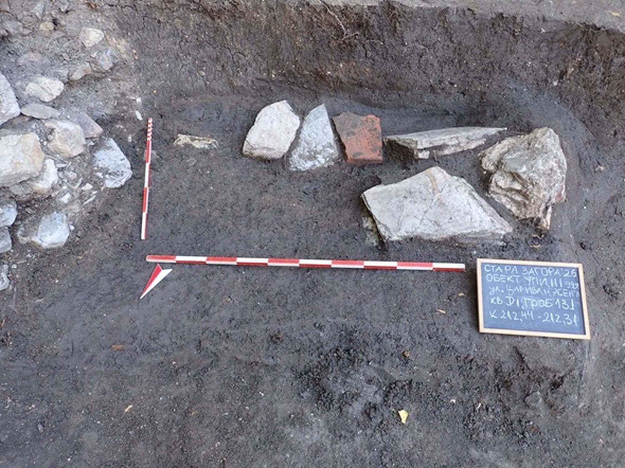 Initial excavation view of the child’s grave, with stones and measuring scales at Augusta Traiana.