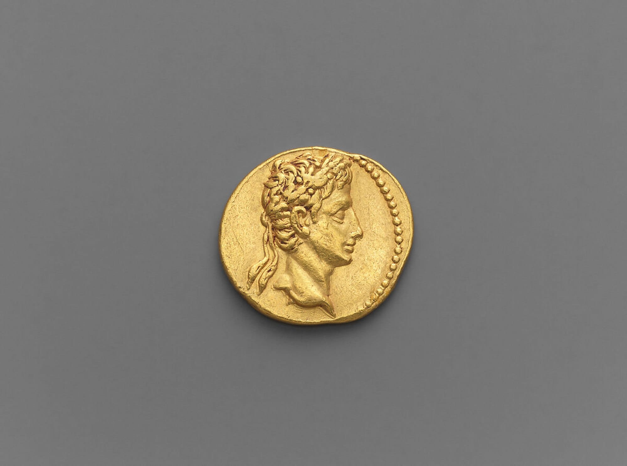 Gold coin showing the oak-wreathed head of Augustus facing right against a grey background.