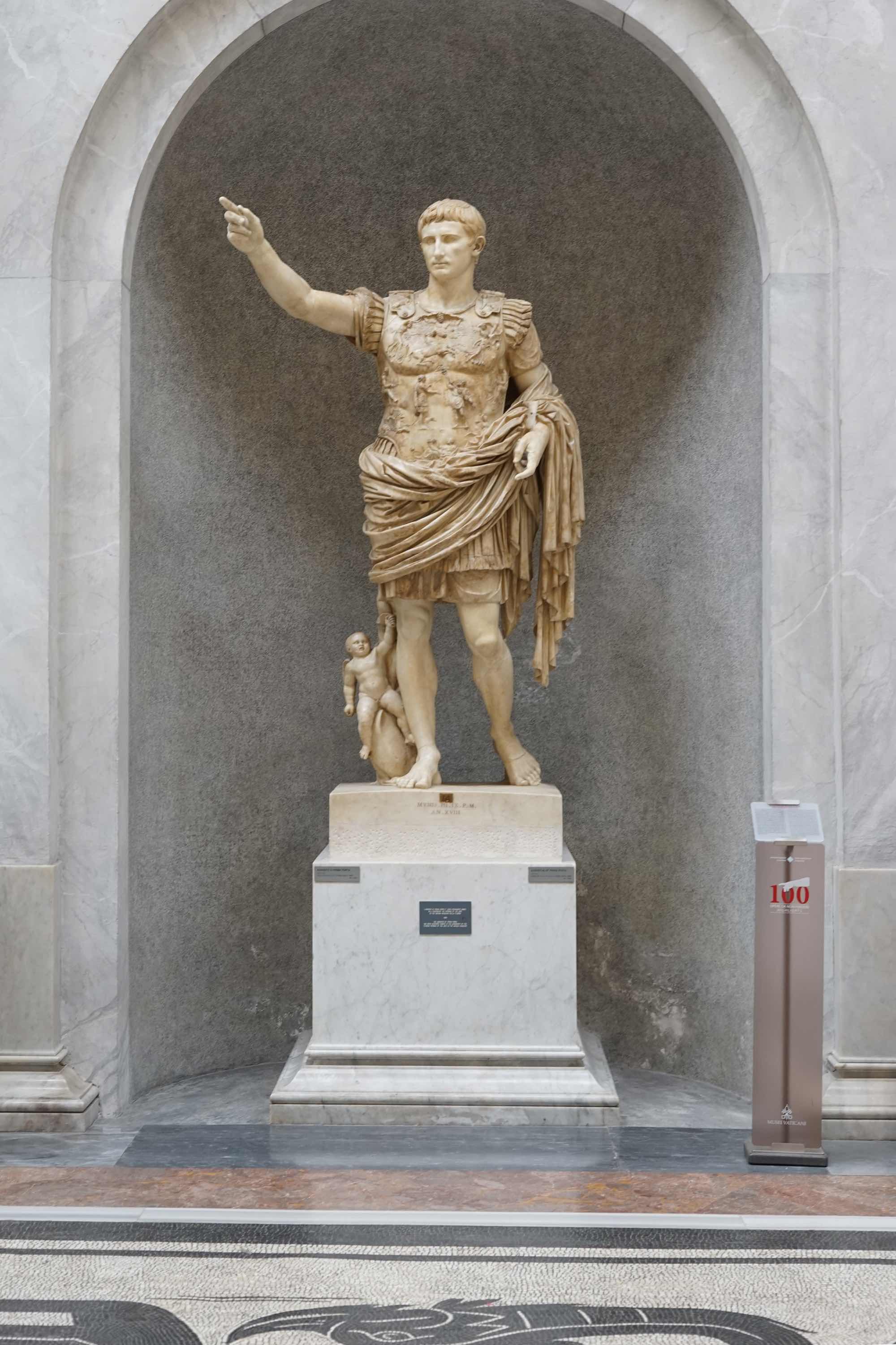 Full marble statue of Augustus of Prima Porta in the Vatican Museums, wearing a decorated military cuirass and raising one arm.