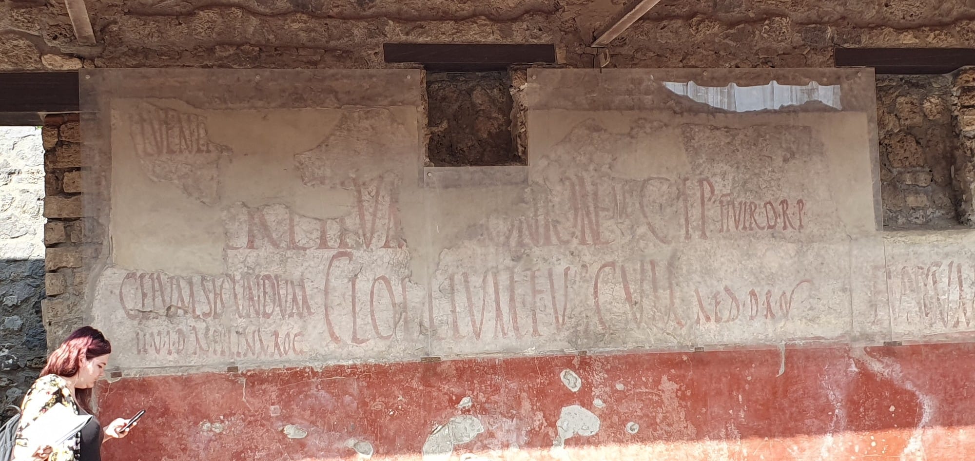 Red painted letters of a Roman election notice survive on pale wall plaster in Pompeii.
