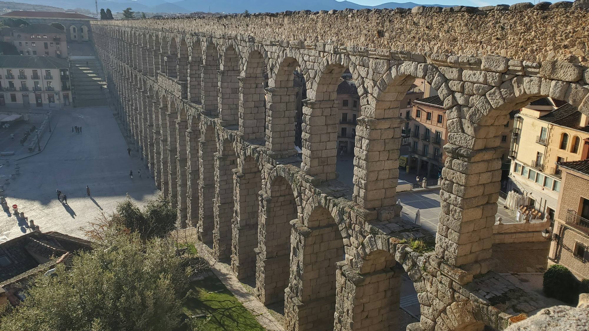 The stone arches of Segovia’s Roman aqueduct cross above a street and landscaped foreground.