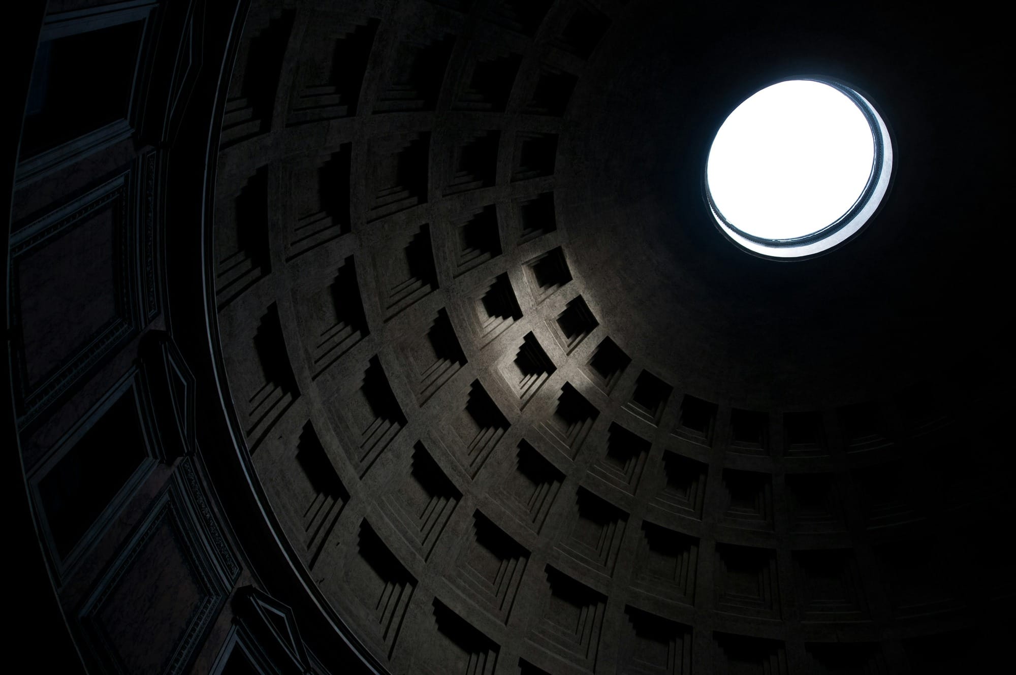 Light enters through the circular oculus above the dark coffered dome of the Pantheon in Rome.