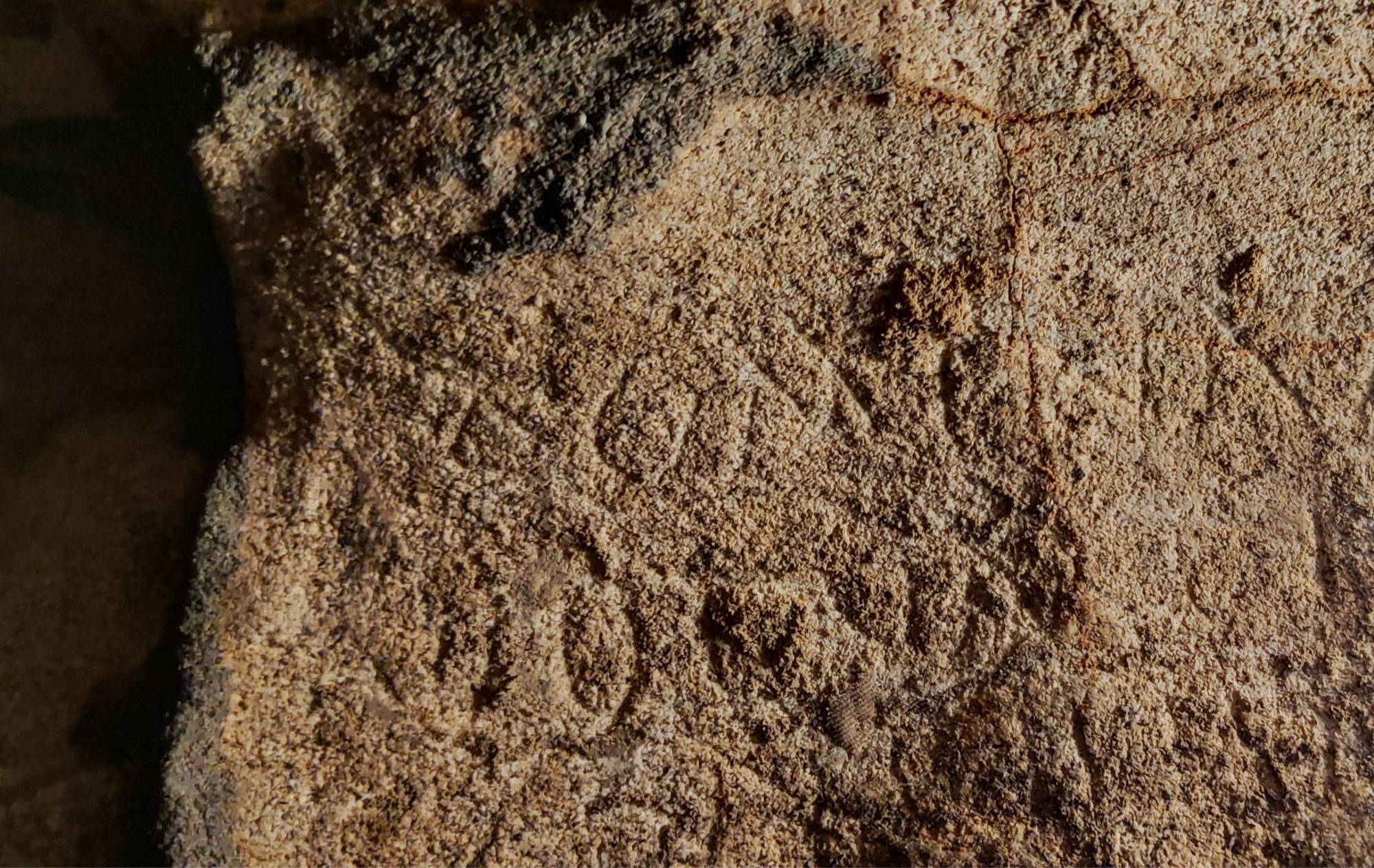 Faint Latin letters scratched into a rough rock surface at Cova Dones.