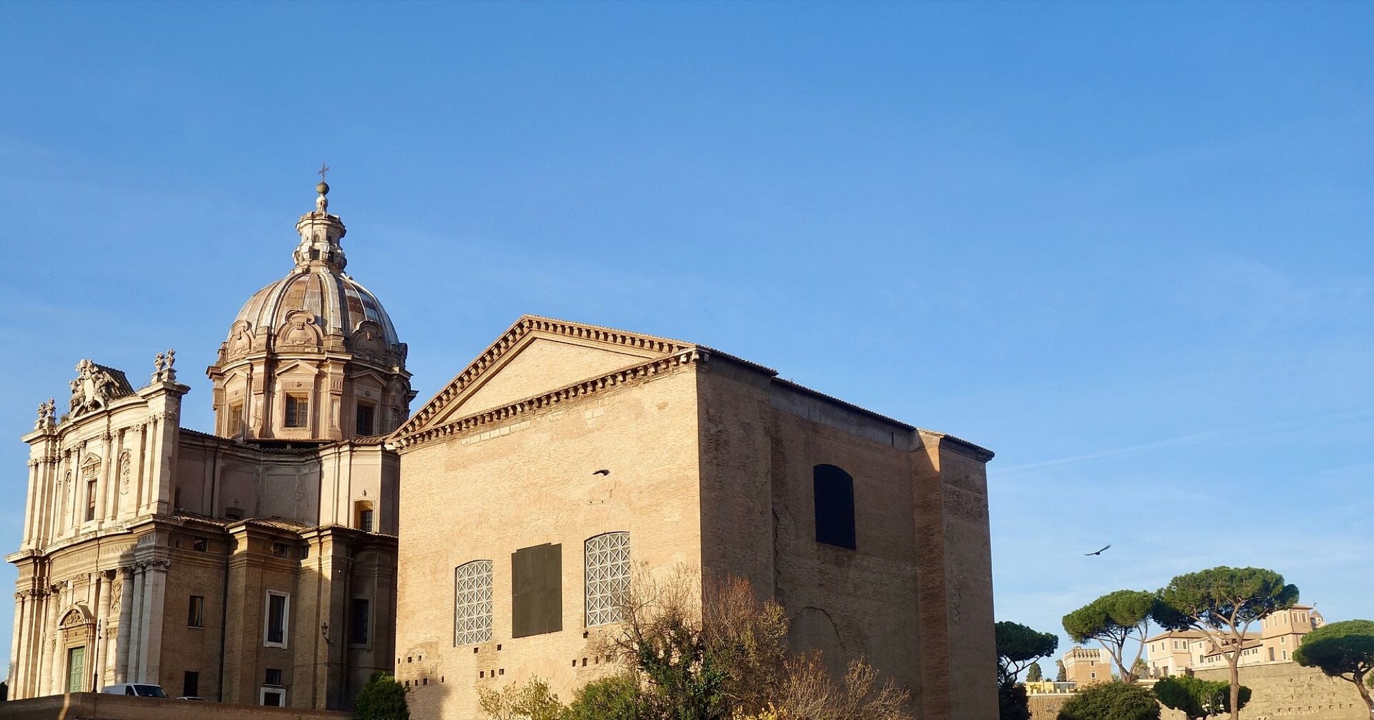 The Curia Julia Senate house in the Roman Forum, with a domed church behind it.