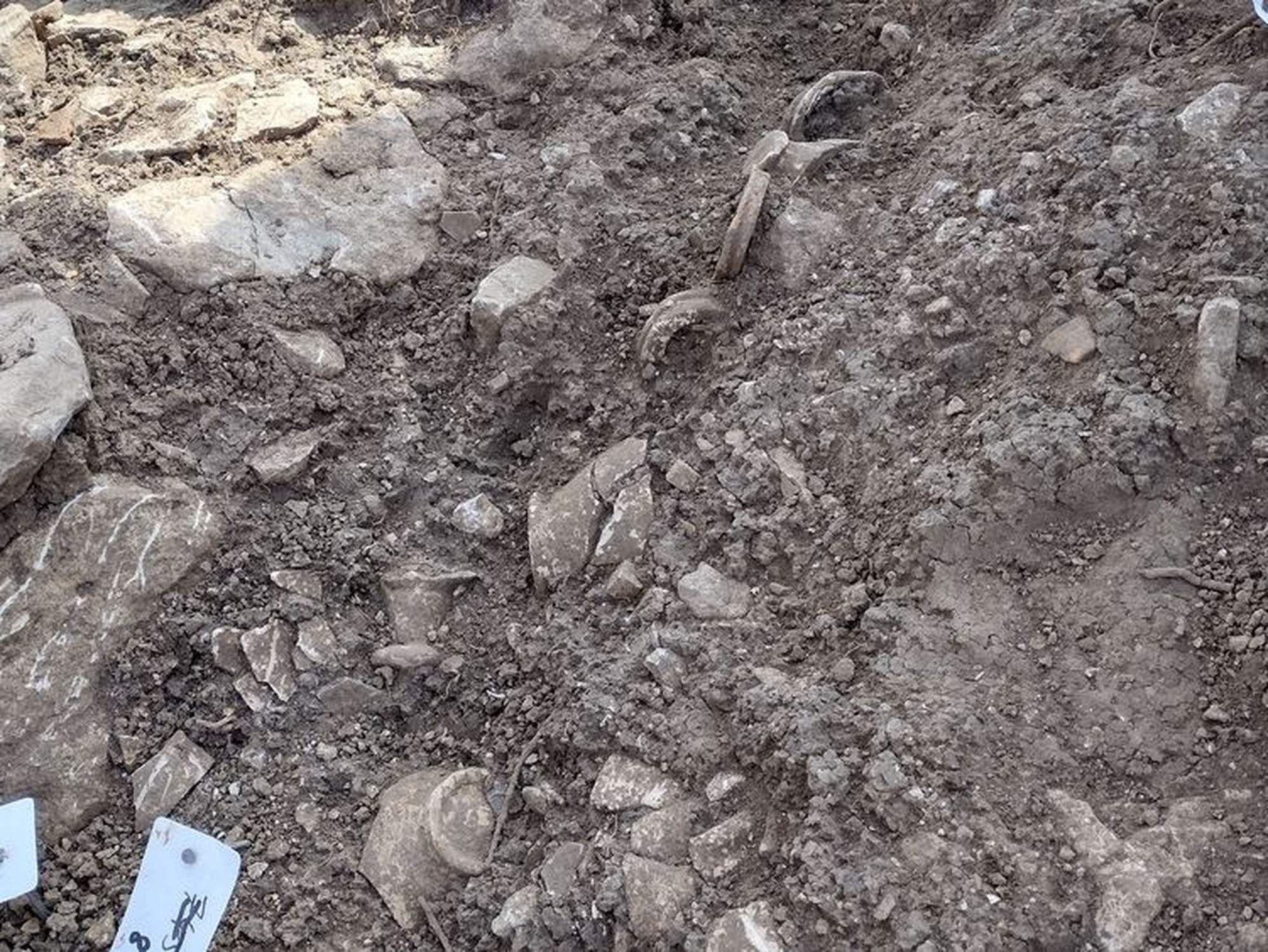 Close view of the excavated water-conduit trench at Grand, with surviving curved iron pipe fittings among the stones.