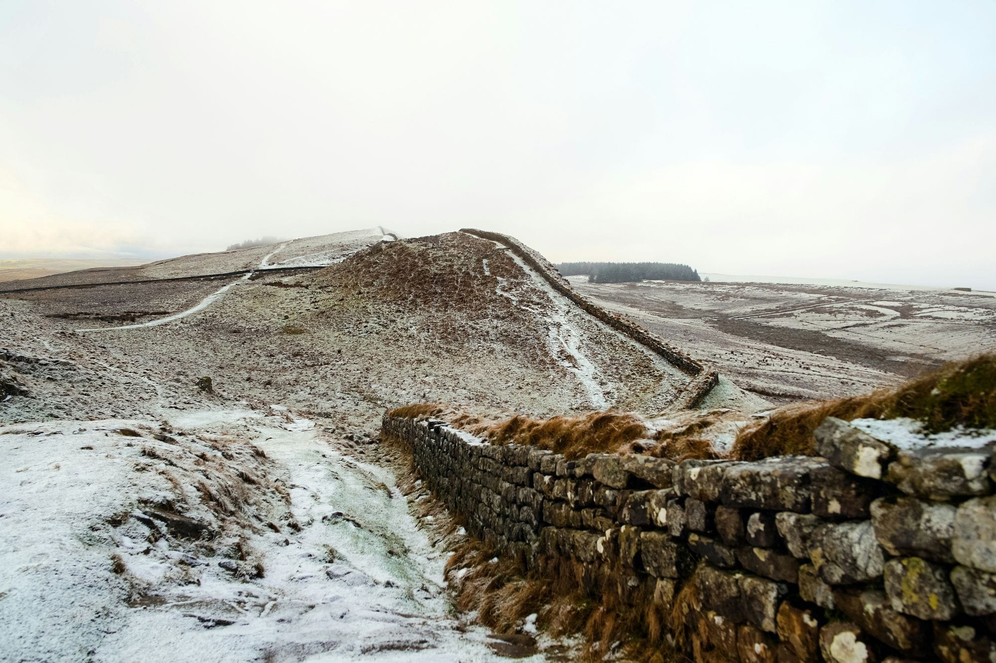 Hadrian’s Wall winding over a snow-dusted ridge, with open countryside on either side.