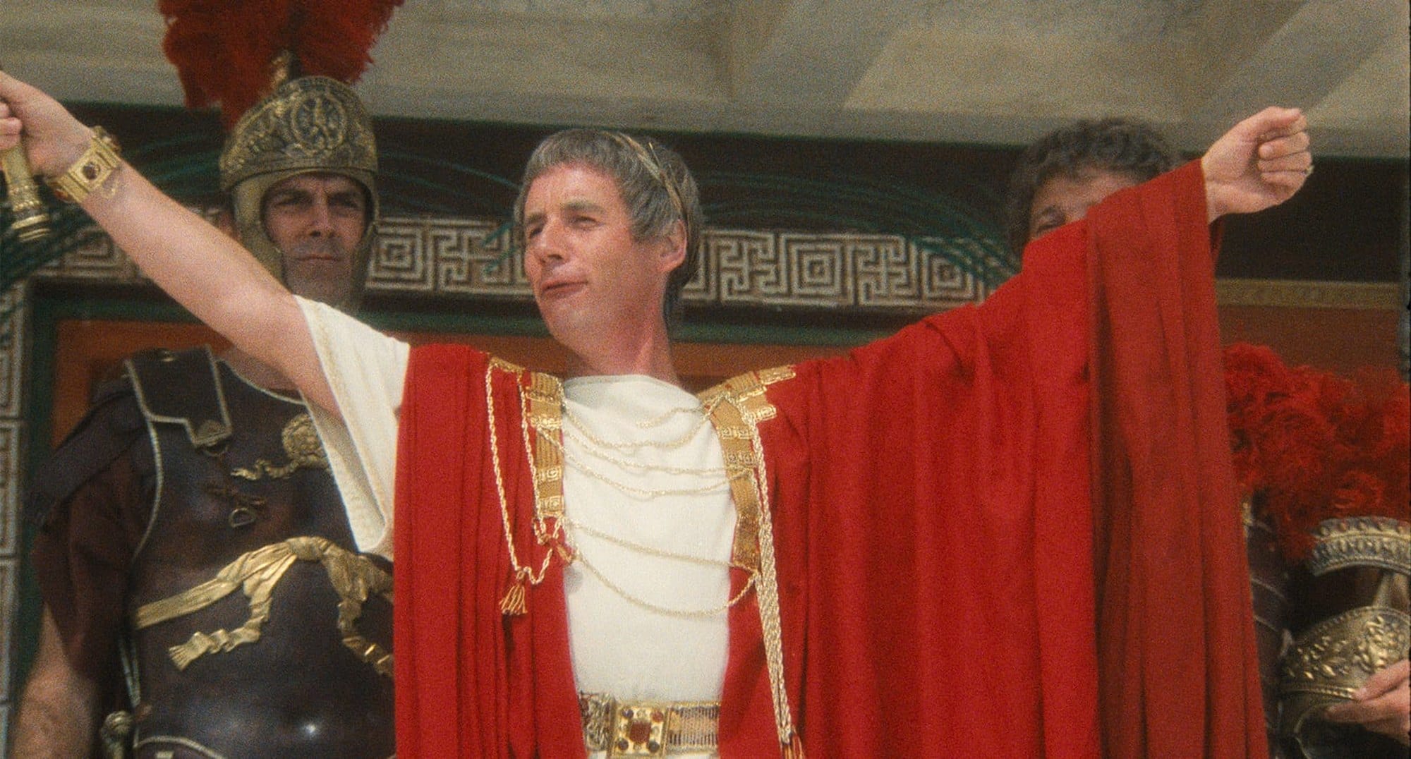 Michael Palin as Pontius Pilate raises his arms between Roman guards in Life of Brian (1979).