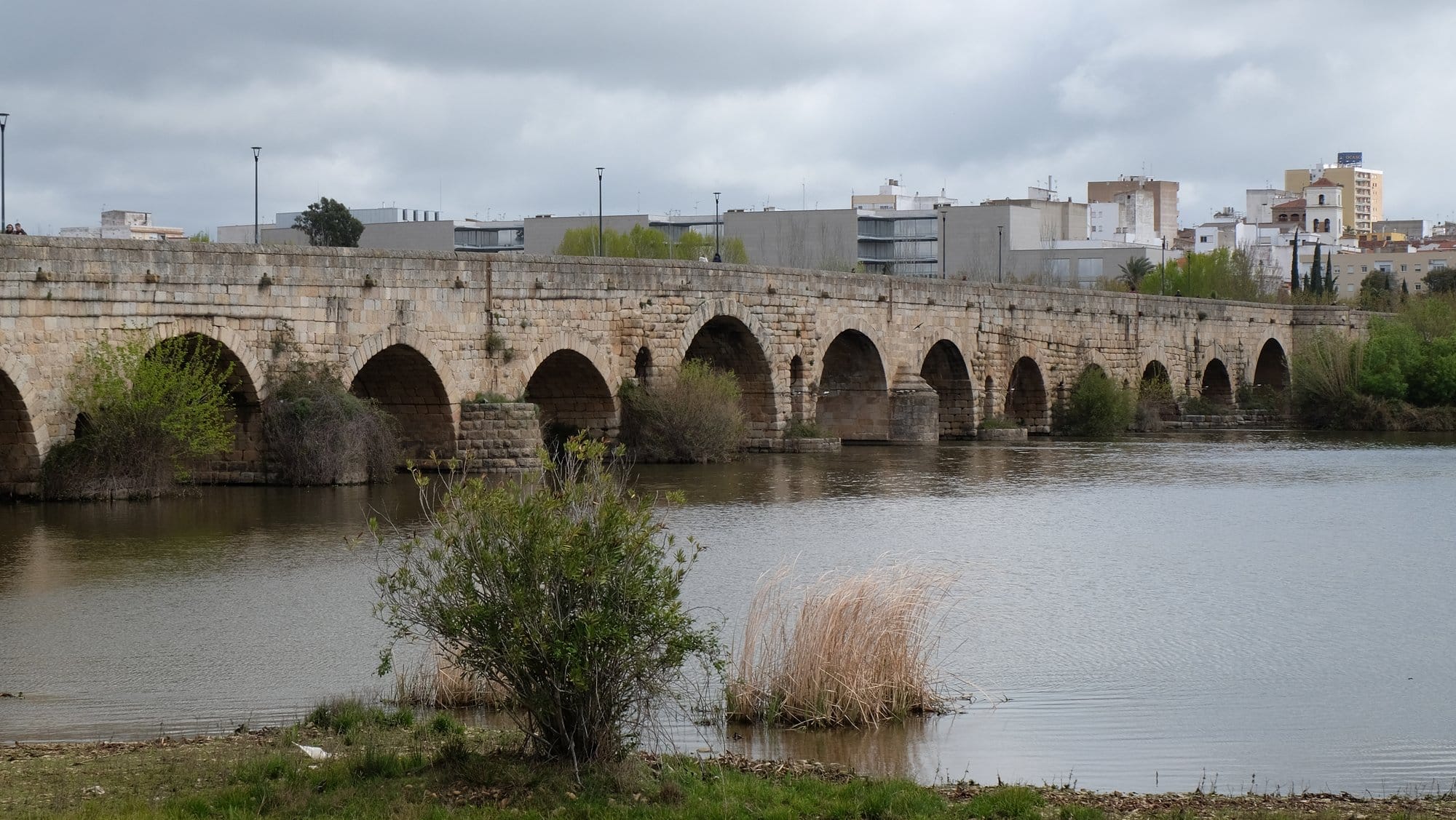 Stone arches of the Roman bridge across the Guadiana at Mérida, with the modern city behind it.