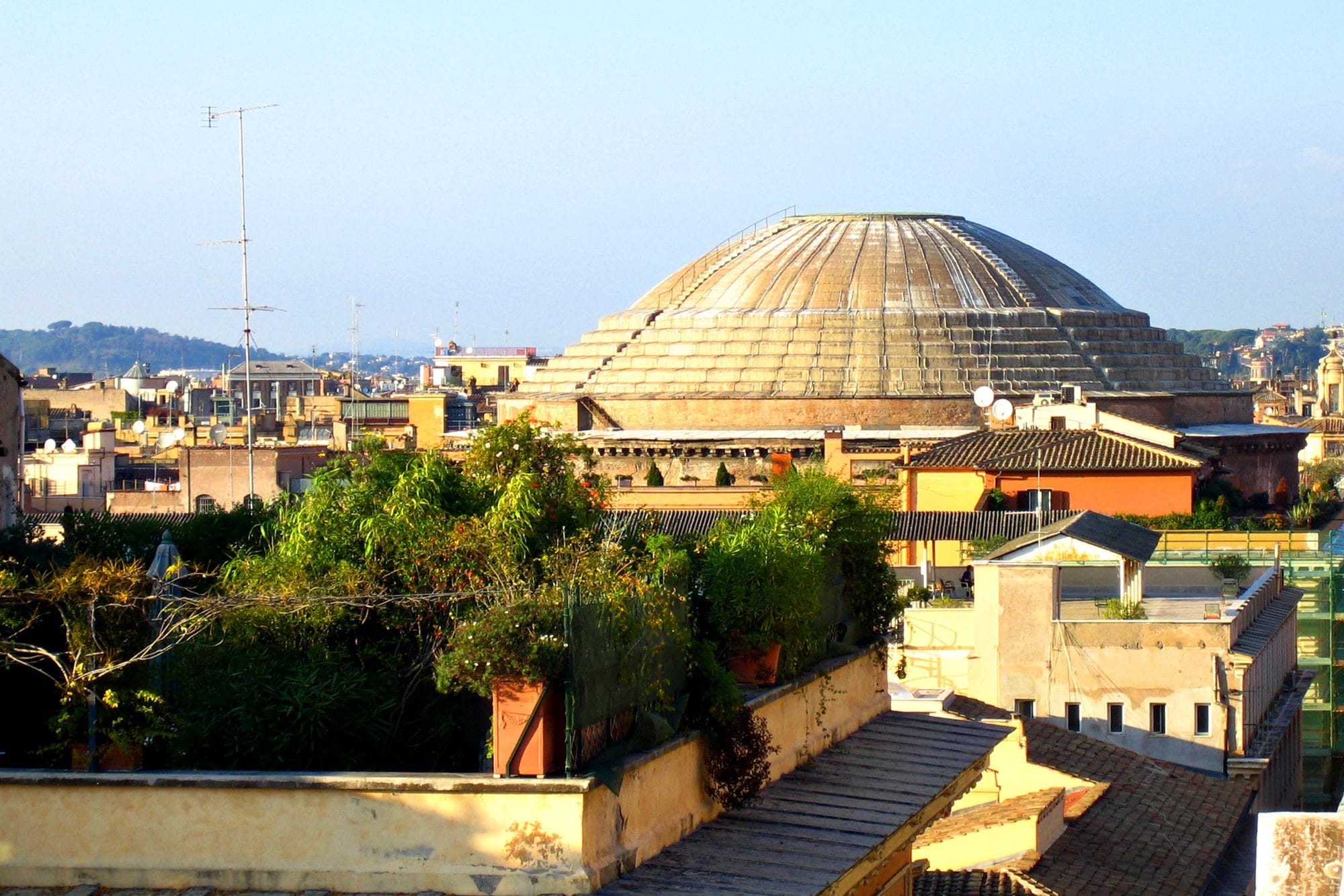 The Pantheon’s broad stepped dome rises behind terracotta rooftops and rooftop gardens in Rome.