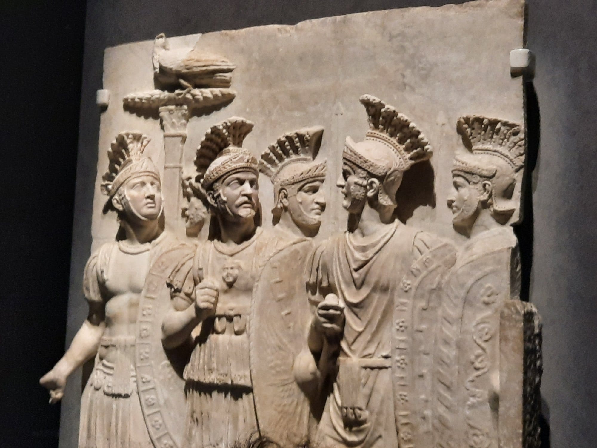 Marble relief of Roman soldiers in parade armour, wearing crested helmets and carrying shields, in the Louvre collection.