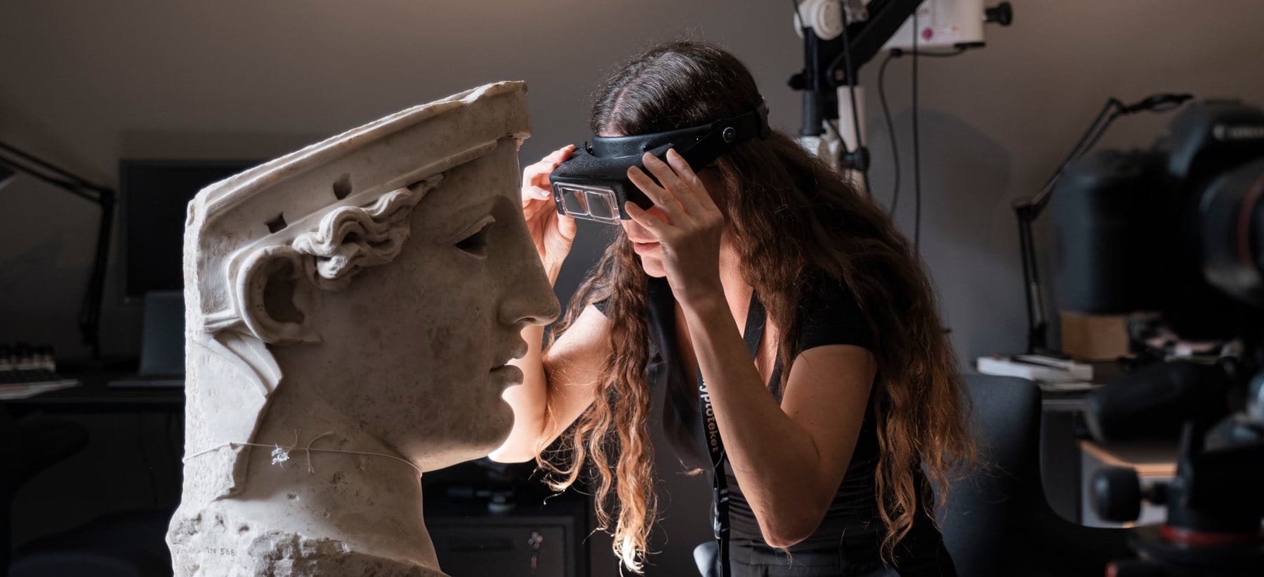 Researcher wearing a magnifying visor examines the face of a Roman marble portrait head.