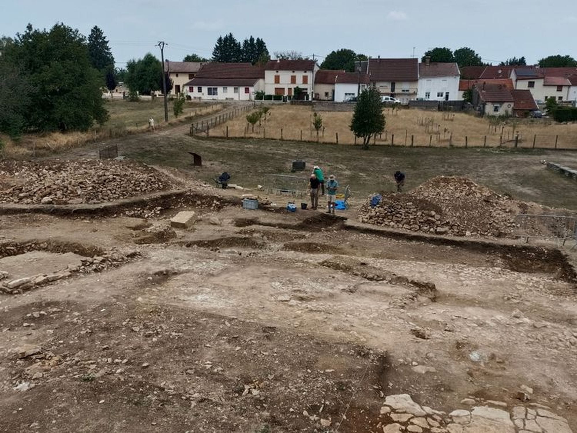 Archaeologists excavate exposed Roman foundations at Grand, with the modern village behind the excavation.