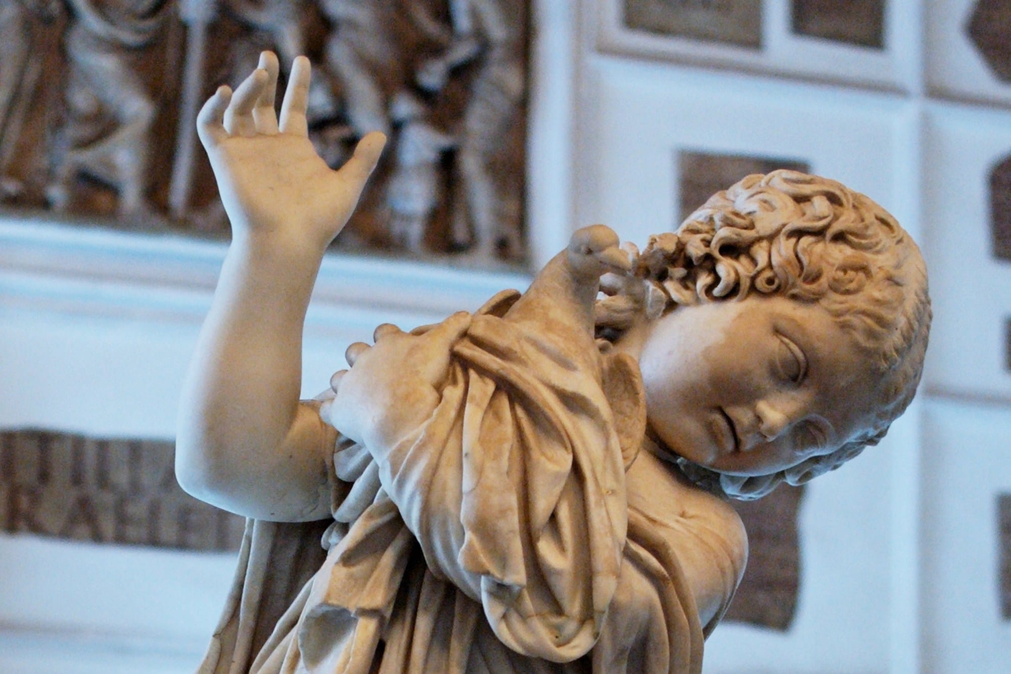 Detail of a Roman marble statue of a curly-haired young girl cradling a dove against her chest.