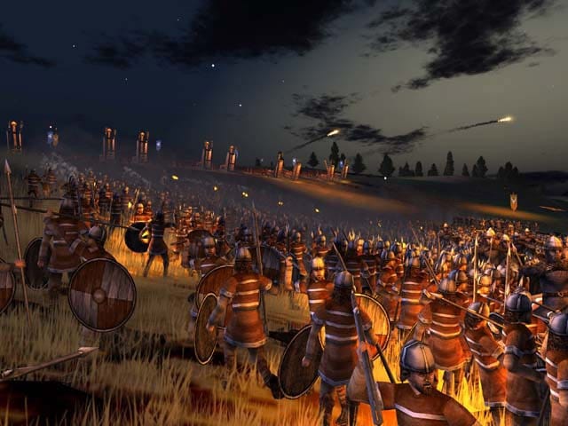 Armoured Roman infantry stand in formation beneath flaming projectiles on a night battlefield in the original Rome: Total War.