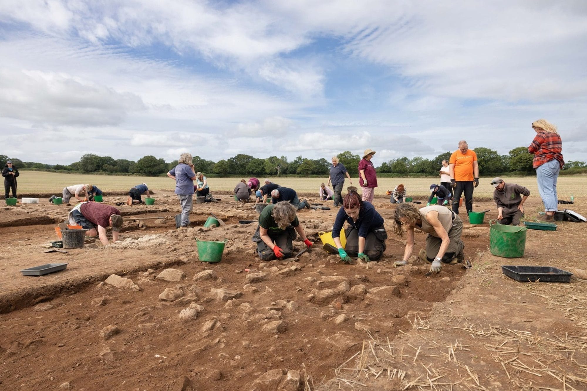 Group of archaeologists and volunteers excavating the Rossett villa site in an open field.