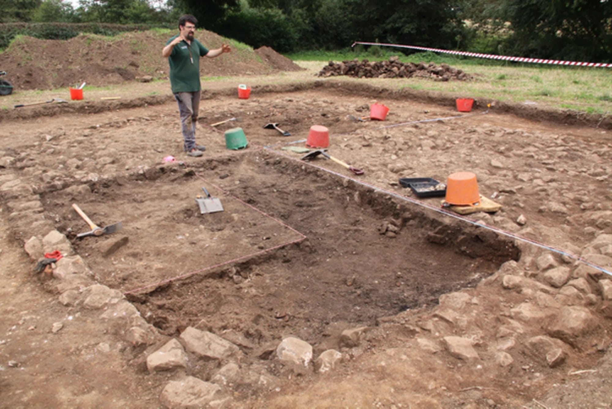 Archaeologist standing by excavated stone remains and soil trenches at Rossett.