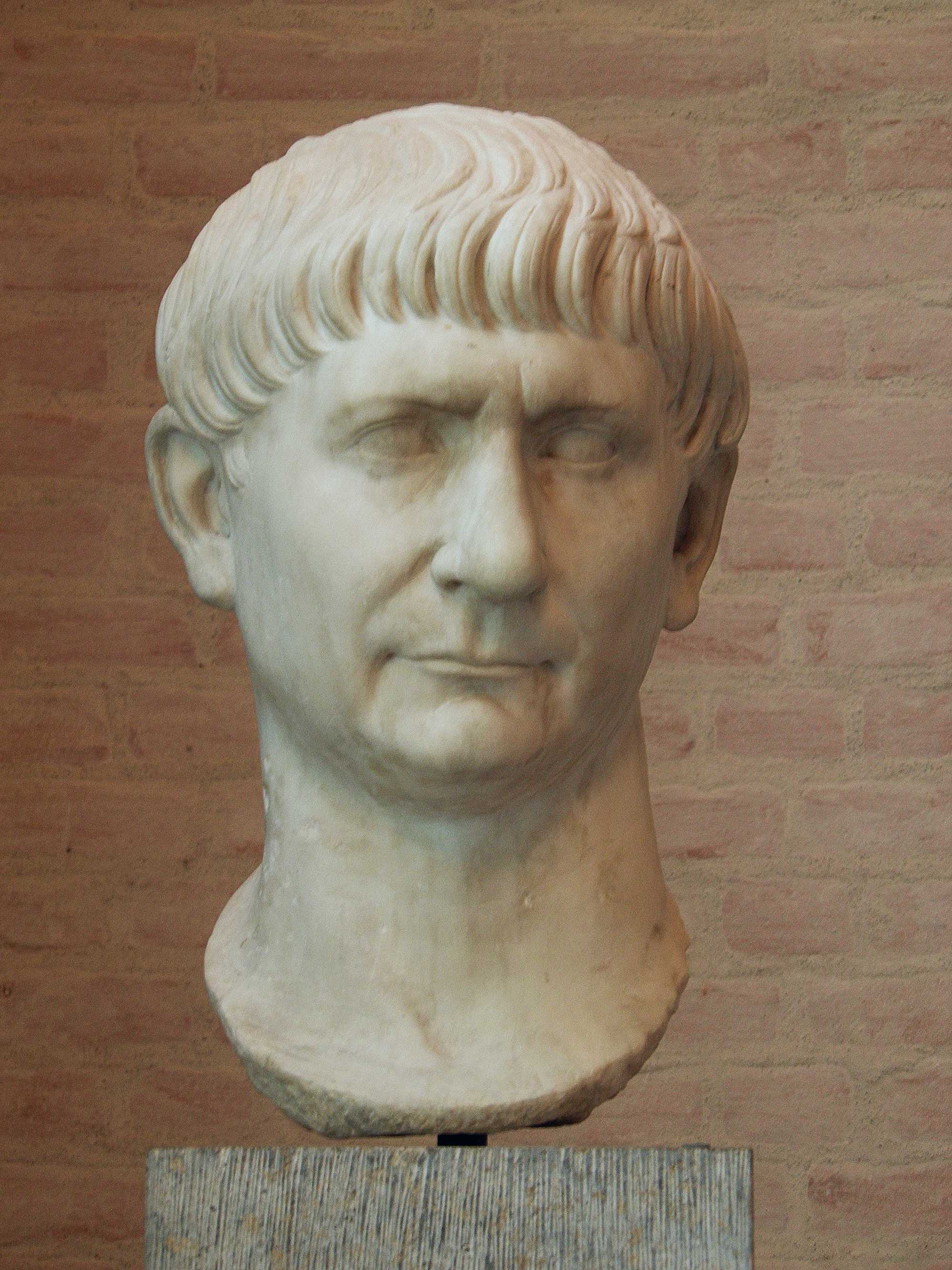 Marble portrait head of Emperor Trajan, with short combed hair, displayed against a brick wall in Munich’s Glyptothek.