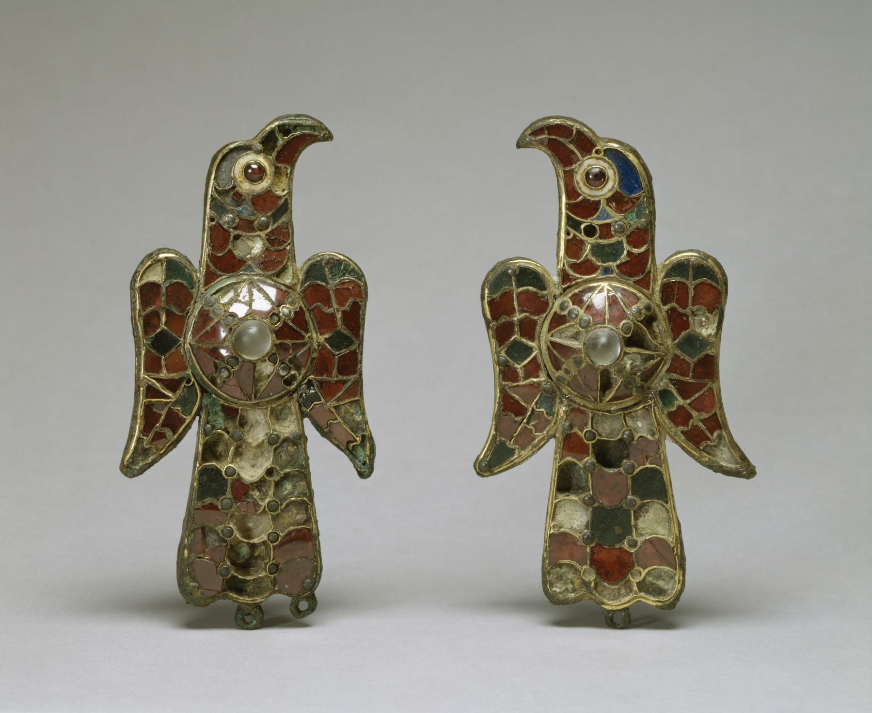 Pair of gold-coloured Visigothic eagle brooches with red, green and blue inlays, displayed side by side.