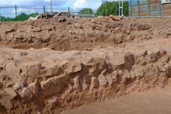 Exposed stonework in an archaeological trench at Caerleon Comprehensive School, with a school fence behind.