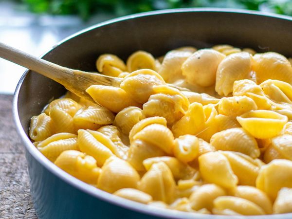 Bowl of modern shell pasta coated in cheese sauce with a wooden spoon; contemporary illustration of macaroni and cheese