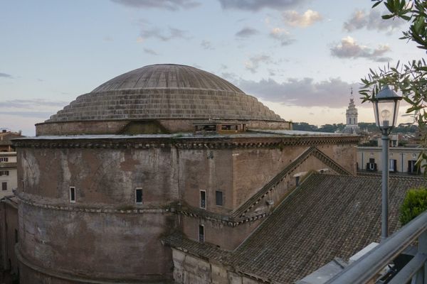 Elevated view of the Pantheon’s stepped dome and brick-faced rotunda among Rome’s rooftops at dusk.