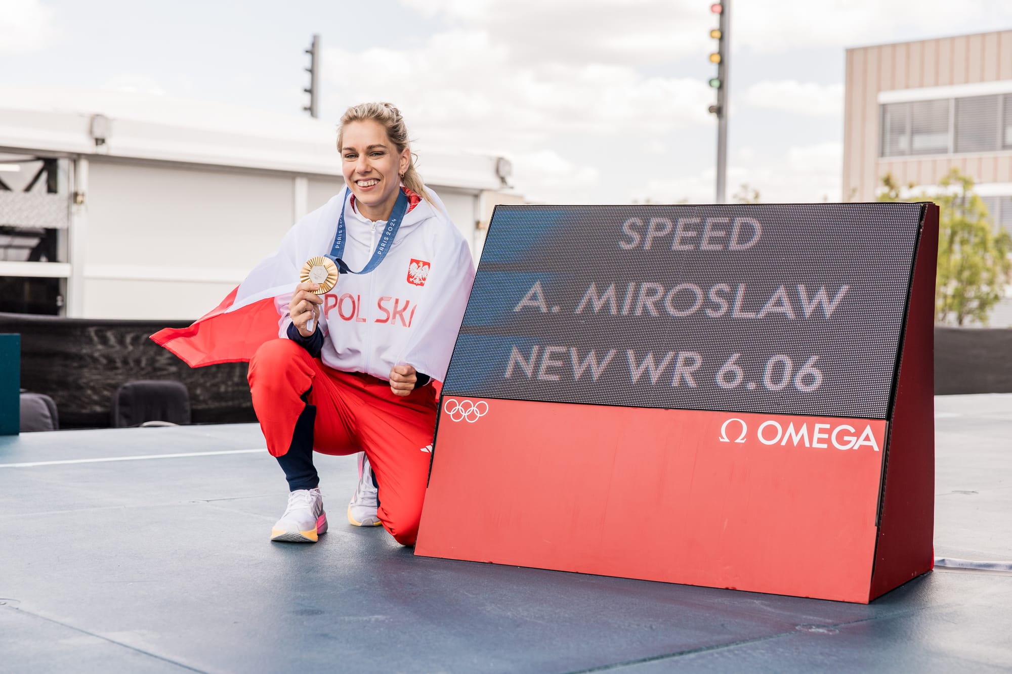 Aleksandra Miroslaw holding. her gold medal next to her World Record time at the Olympics.