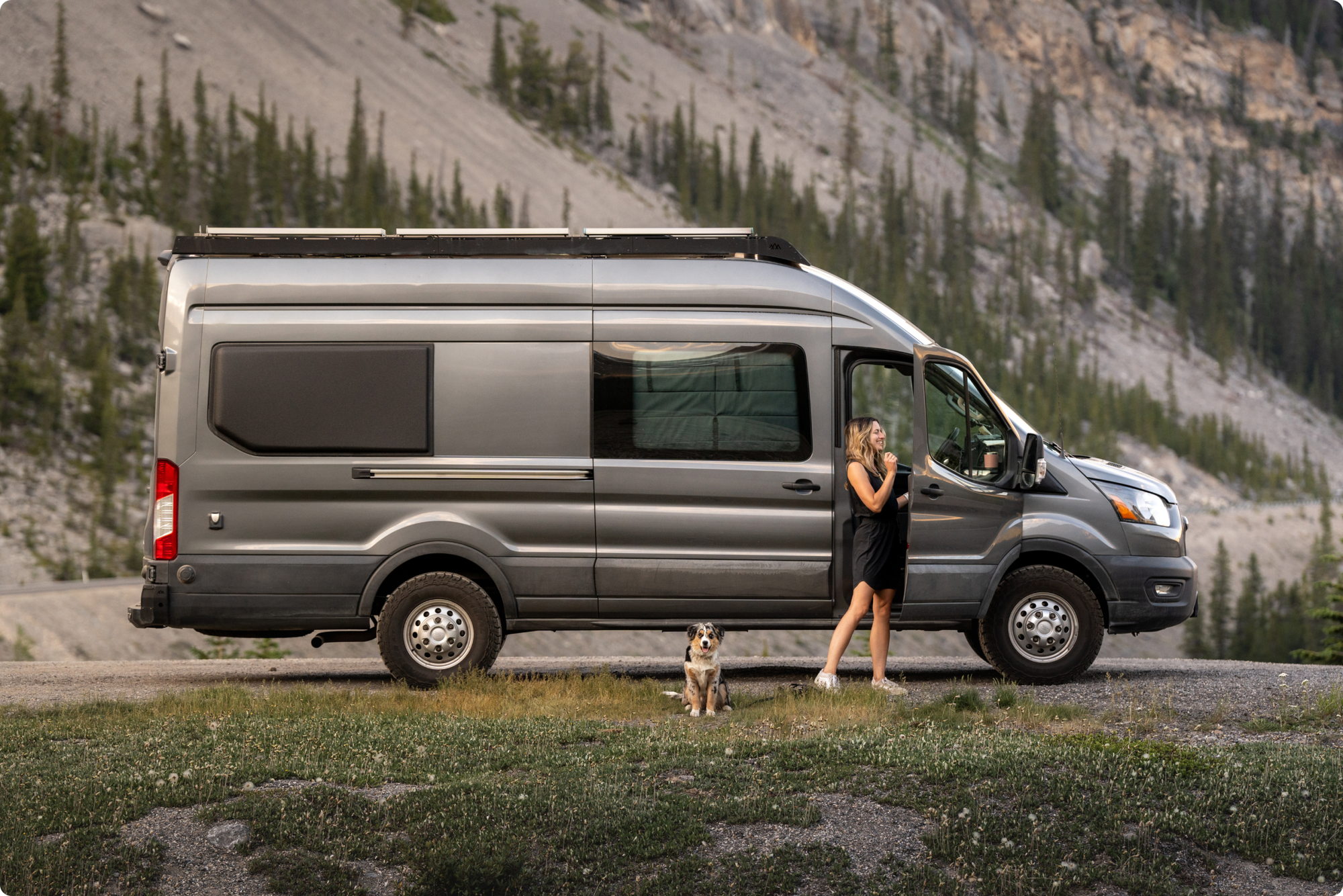 Woman and dog next to a campervan at the foot of a mountain