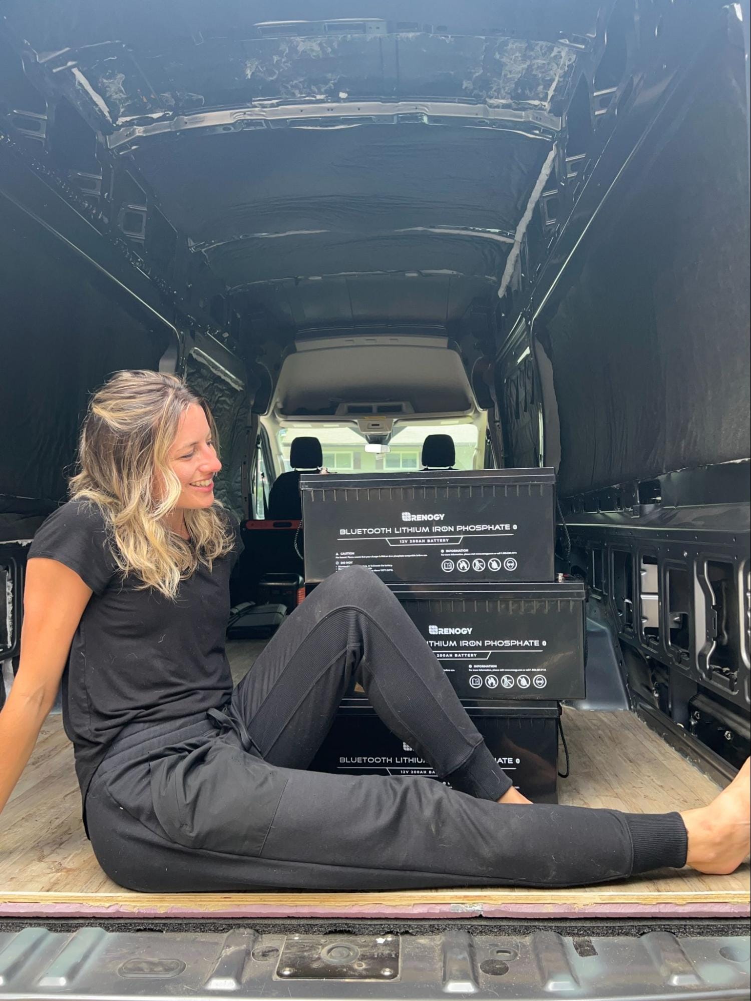 Young woman sitting in the back of a stripped campervan with a stack of black batteries