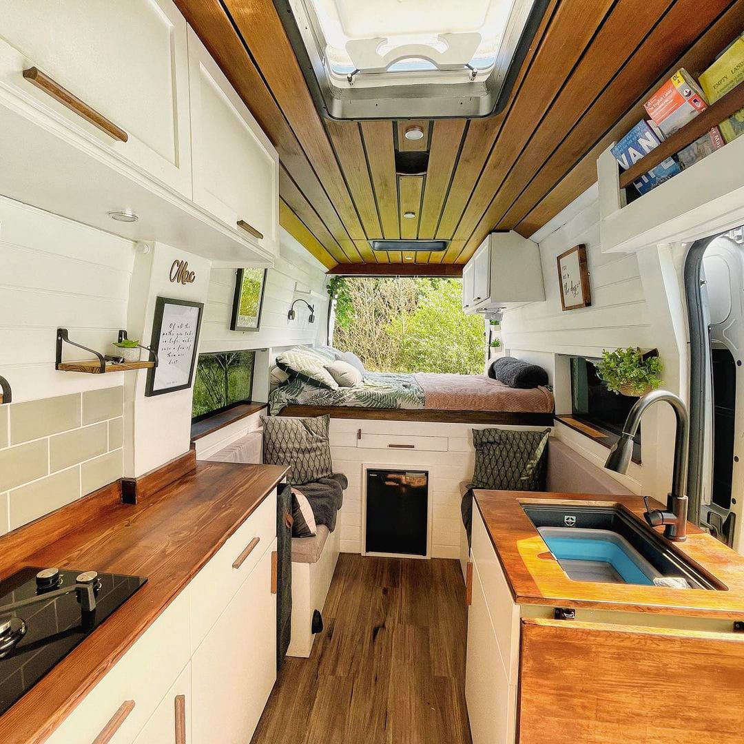 Interior of a campervan with large skylight over a kitchenette and neatly made bed beyond