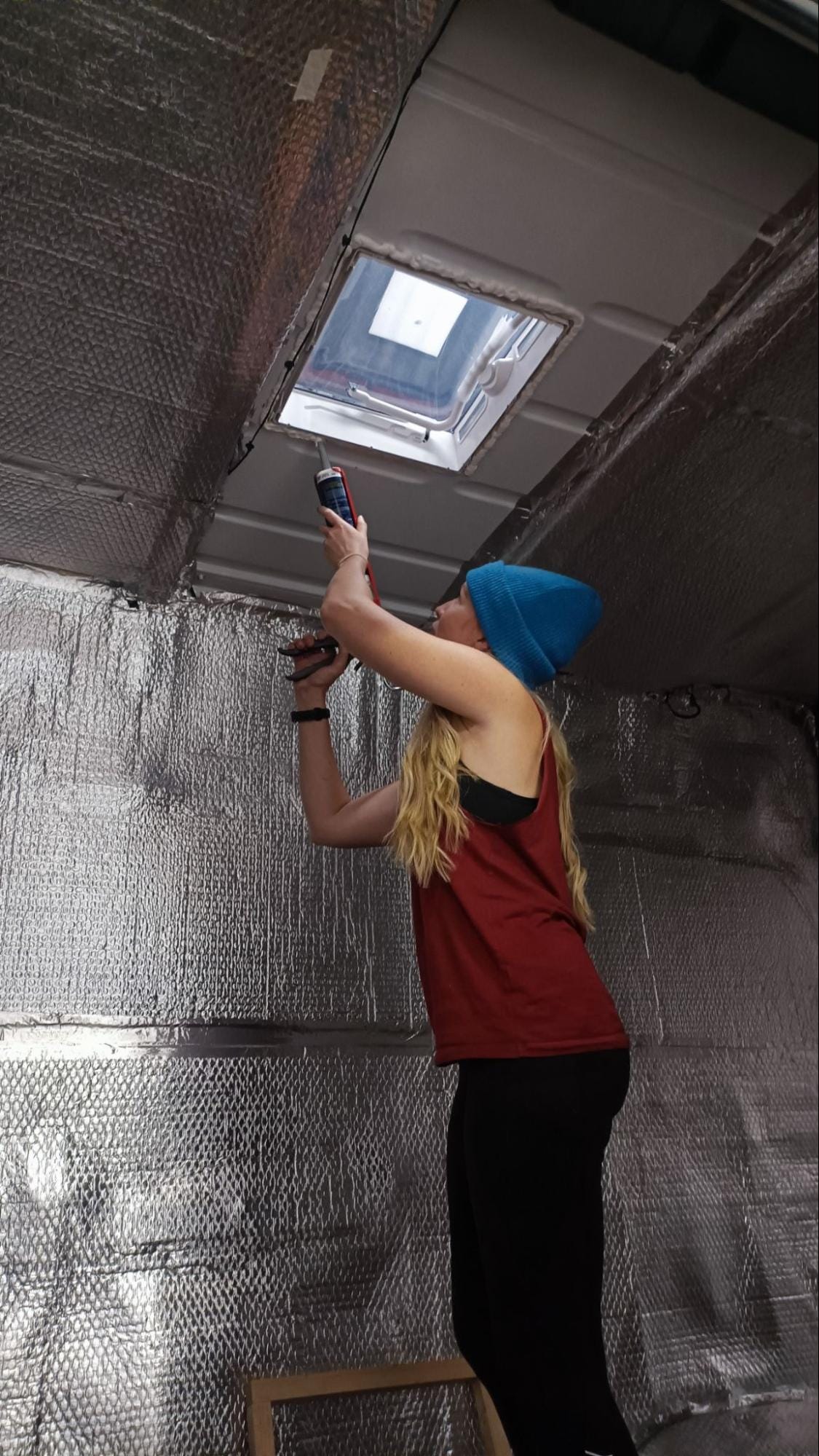 Young woman in a beanie drilling into the ceiling of a campervan