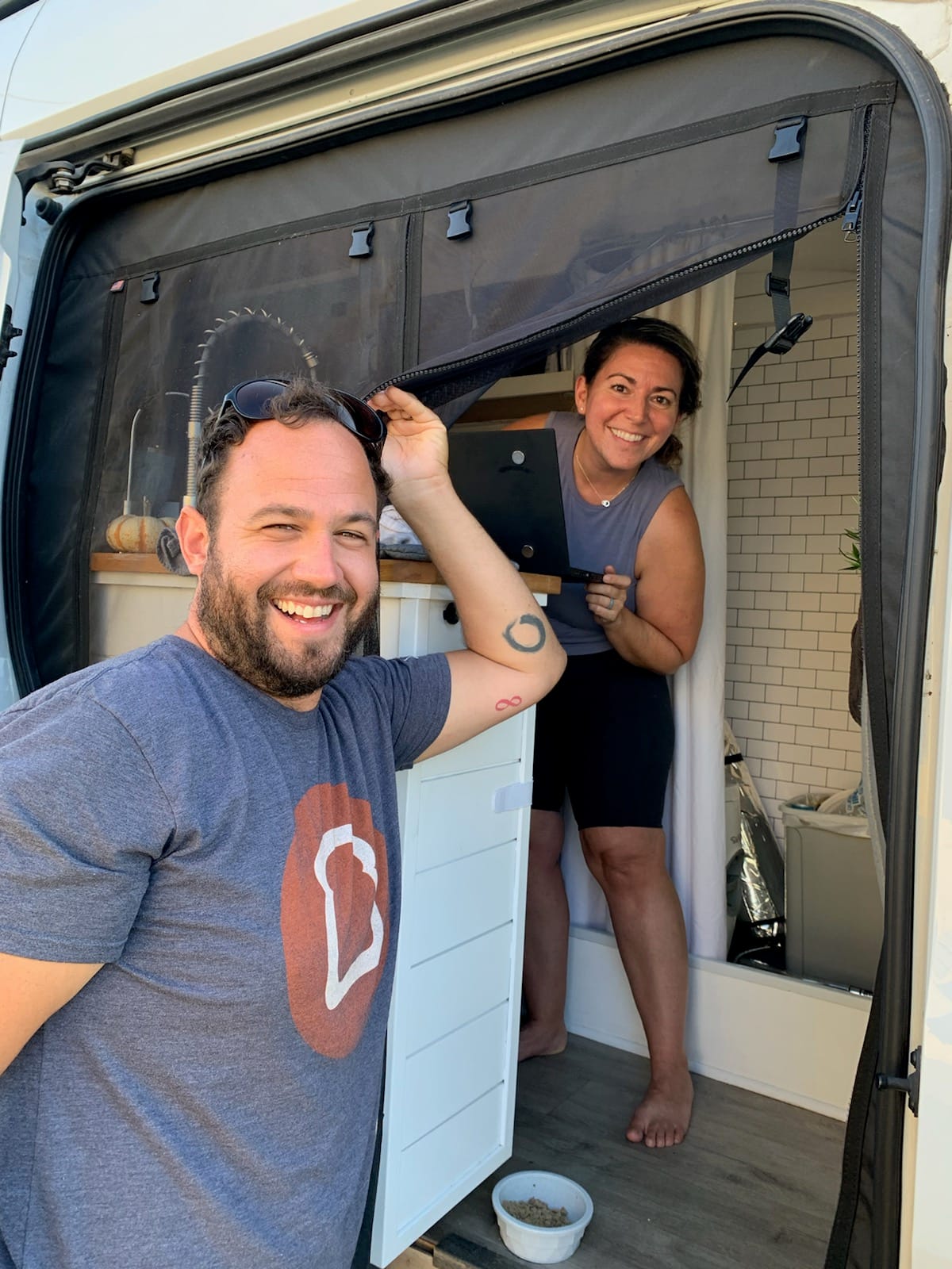 Vanlife couple standing in the open doorway of a van posing for a picture