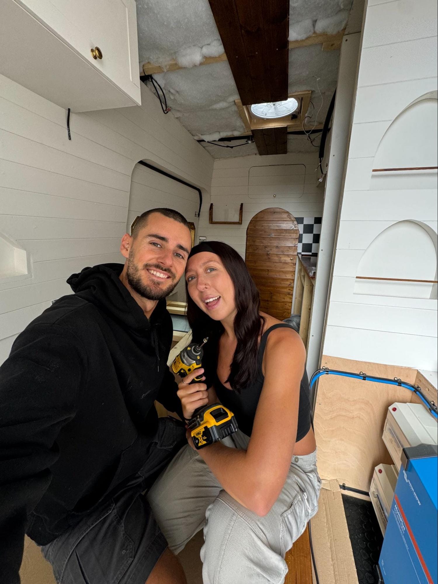 Young couple in the back of a partially converted campervan posing for a picture
