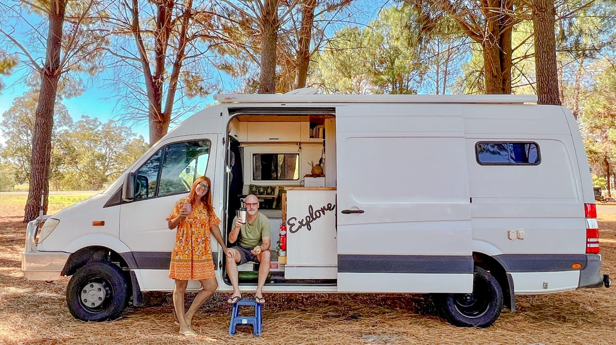 Vanlife couple sitting in the doorway of a white Sprinter van