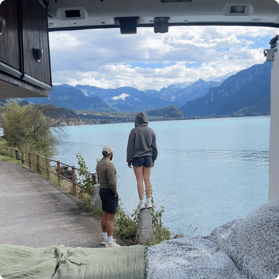 View of a lake and mountains from the back of a campervan with a couple looking out over the water