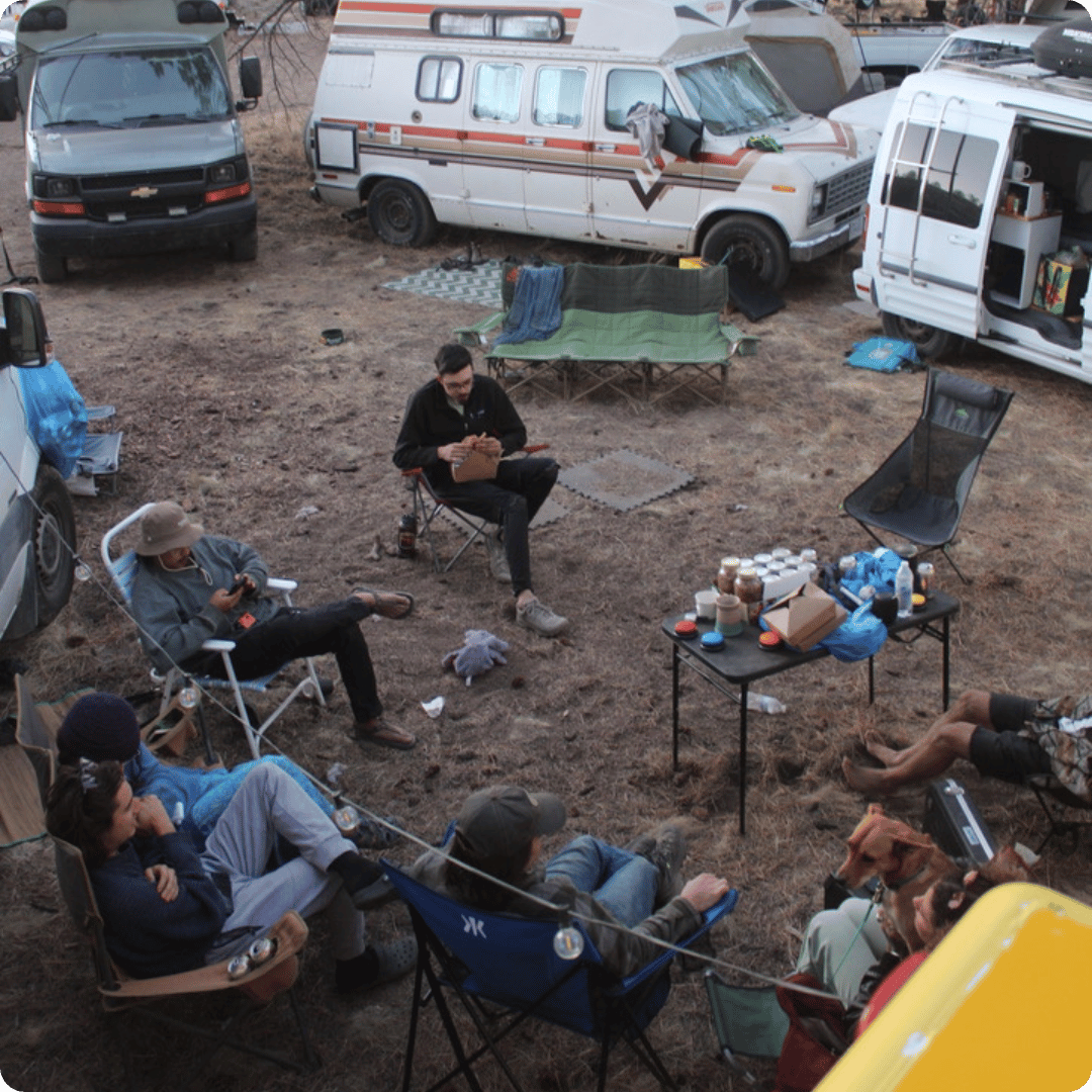Group of people sitting outdoors in camper chairs with campervans surrounding them