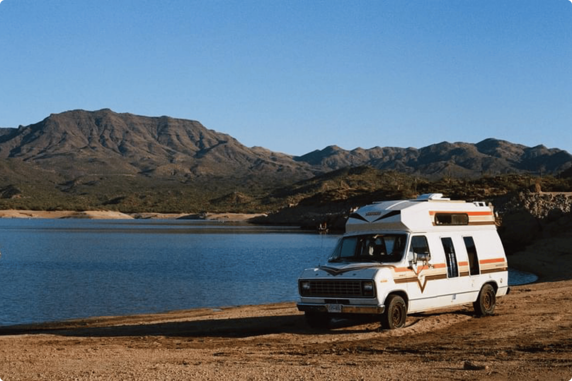 Retro looking campervan parked in the dirt beside a lake