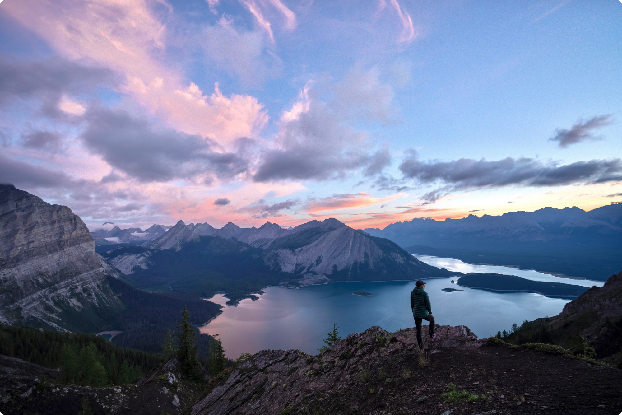 Woman standing on a mountain top overlooking a vast lake and mountainous region at sunrise