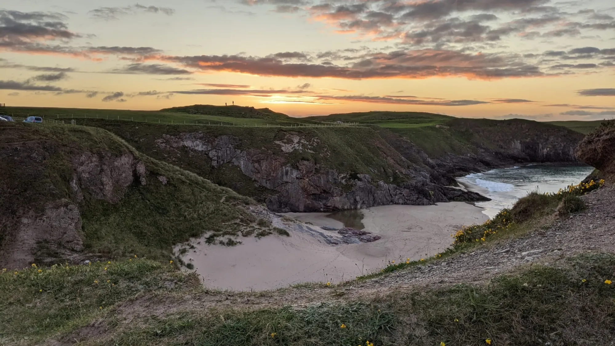 A small bay surrounded by grassy cliffs with calm waters at sunset