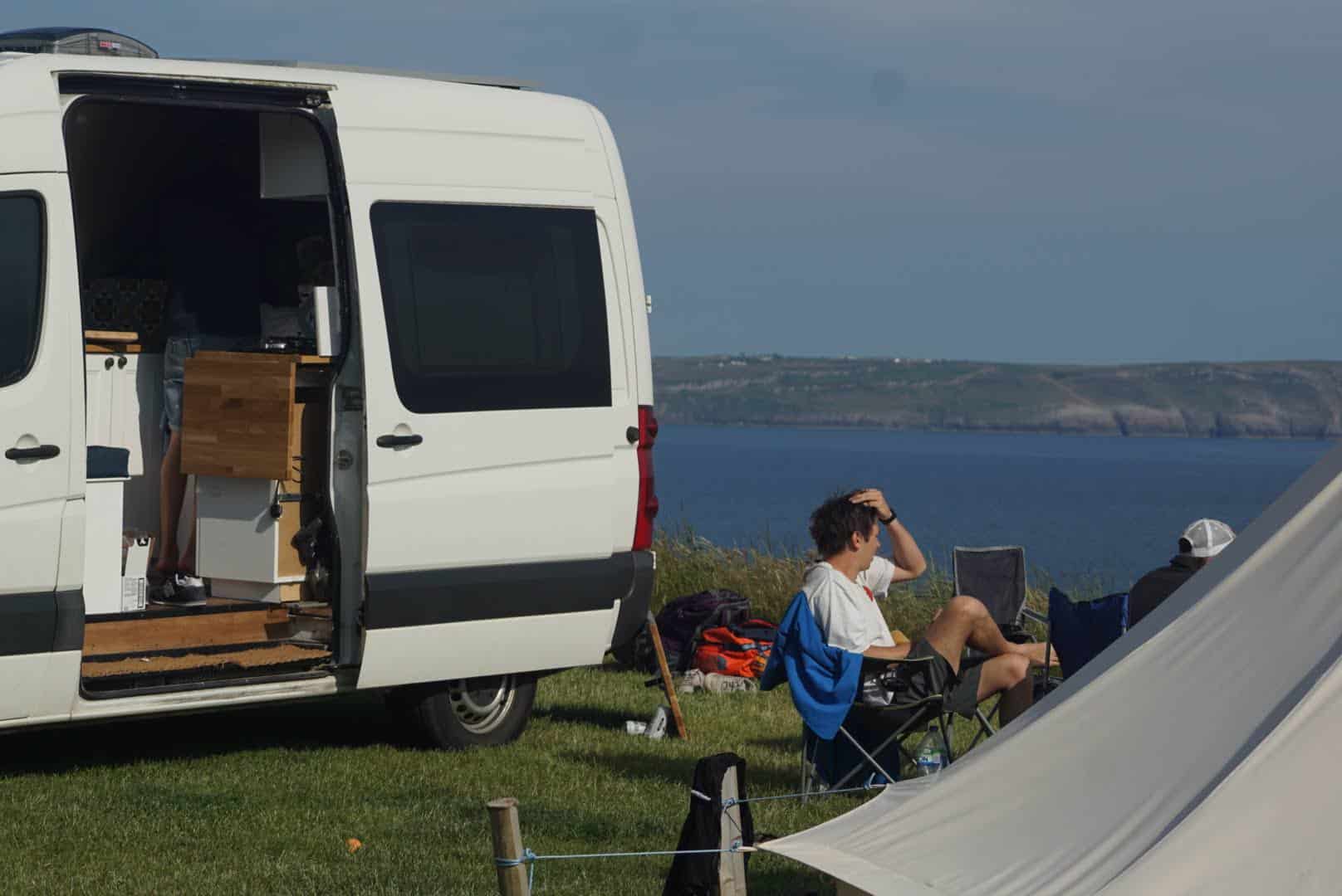 White campervan with man in chair living off grid near a body of water