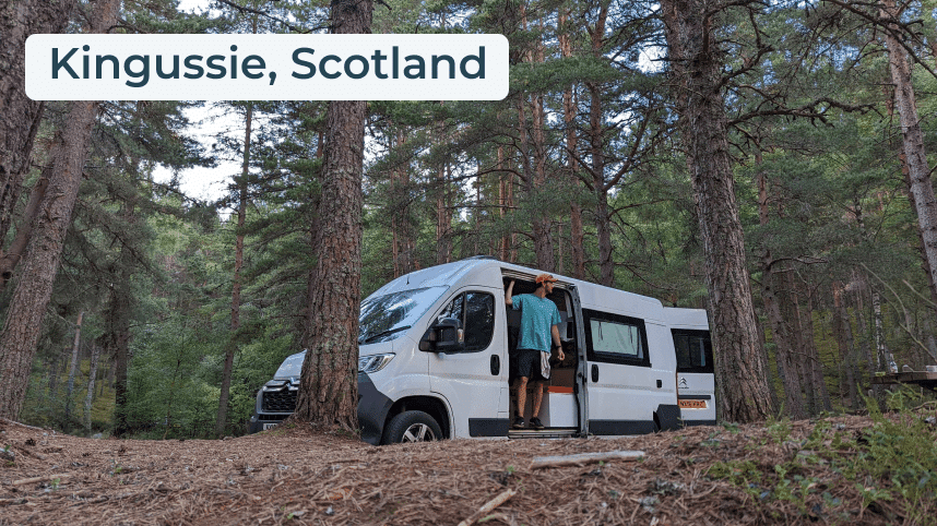 White campervan parked in the woods with man standing in the side doorway