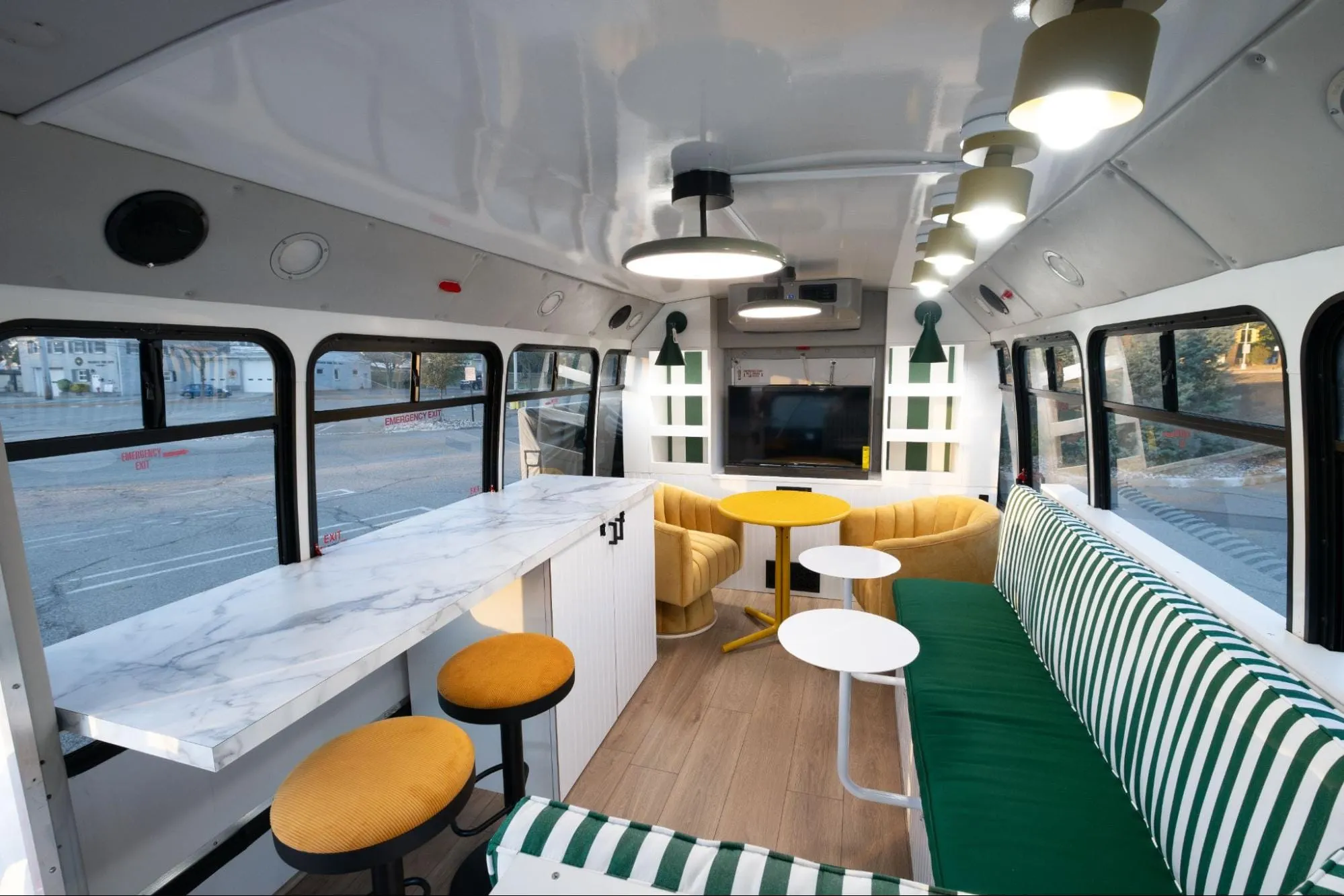 plush interior of a converted school bus with large green upholstered bench and yellow arm chairs in the rear