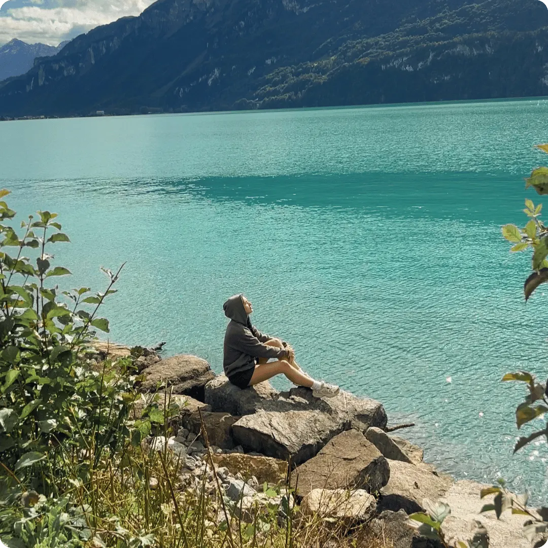 Woman sitting on a rock next to a turquoise lake