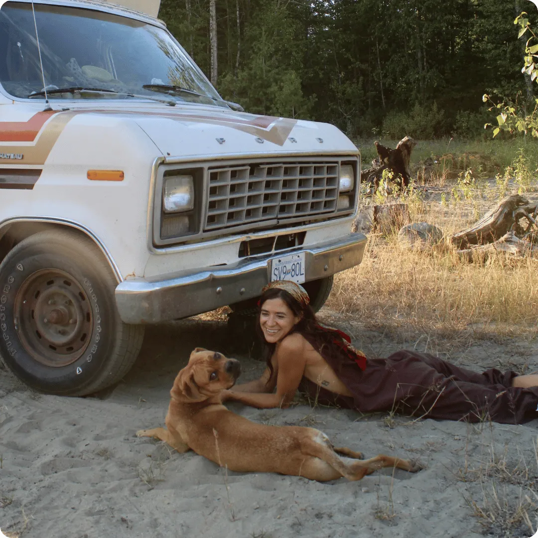 Woman and dog lying in the dirt beside a campervan