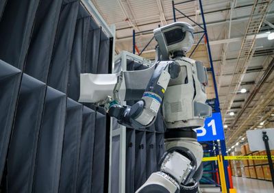 Boston Dynamics Atlas handles an industrial part inside a factory work cell.
